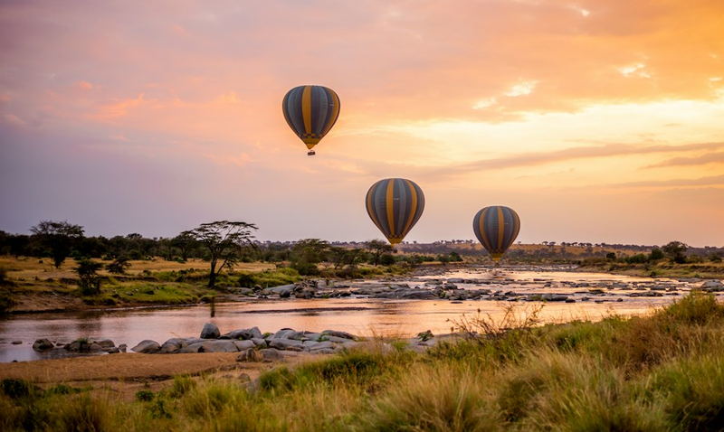 Three hot air balloons drifting over a river at sunrise